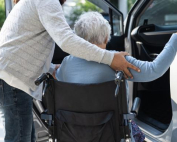 Lady in a wheelchair being helped into a car
